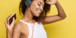 Lifestyle Concept - Portrait of beautiful African American woman joyful listening to music on mobile phone. Yellow pastel studio background. Copy Space.