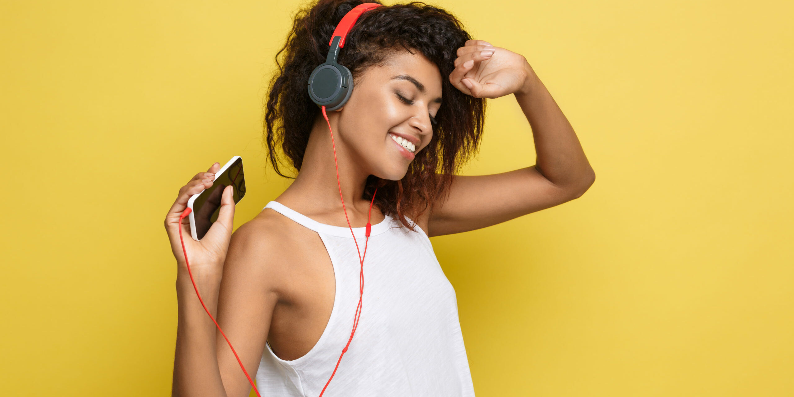 Lifestyle Concept - Portrait of beautiful African American woman joyful listening to music on mobile phone. Yellow pastel studio background. Copy Space.