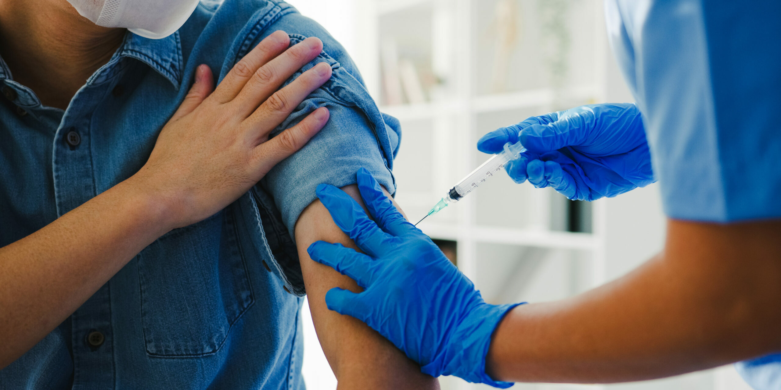 Young Asia lady nurse giving Covid-19 or flu antivirus vaccine shot to senior male patient wear face mask protection from virus disease at health clinic or hospital office. Vaccination concept.